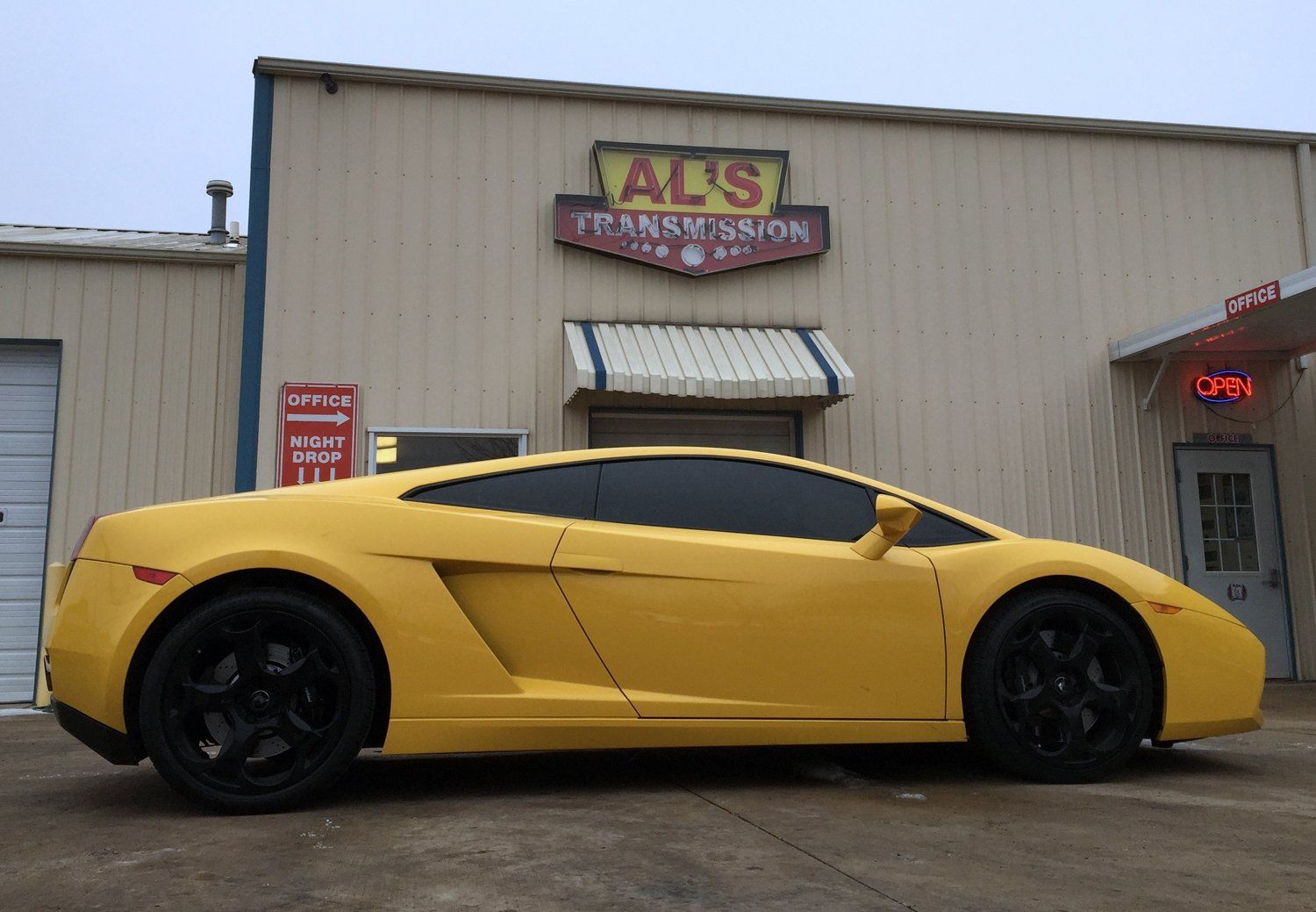 Yellow sports car parked outside an auto repair shop with an ATS Transmission sign.
