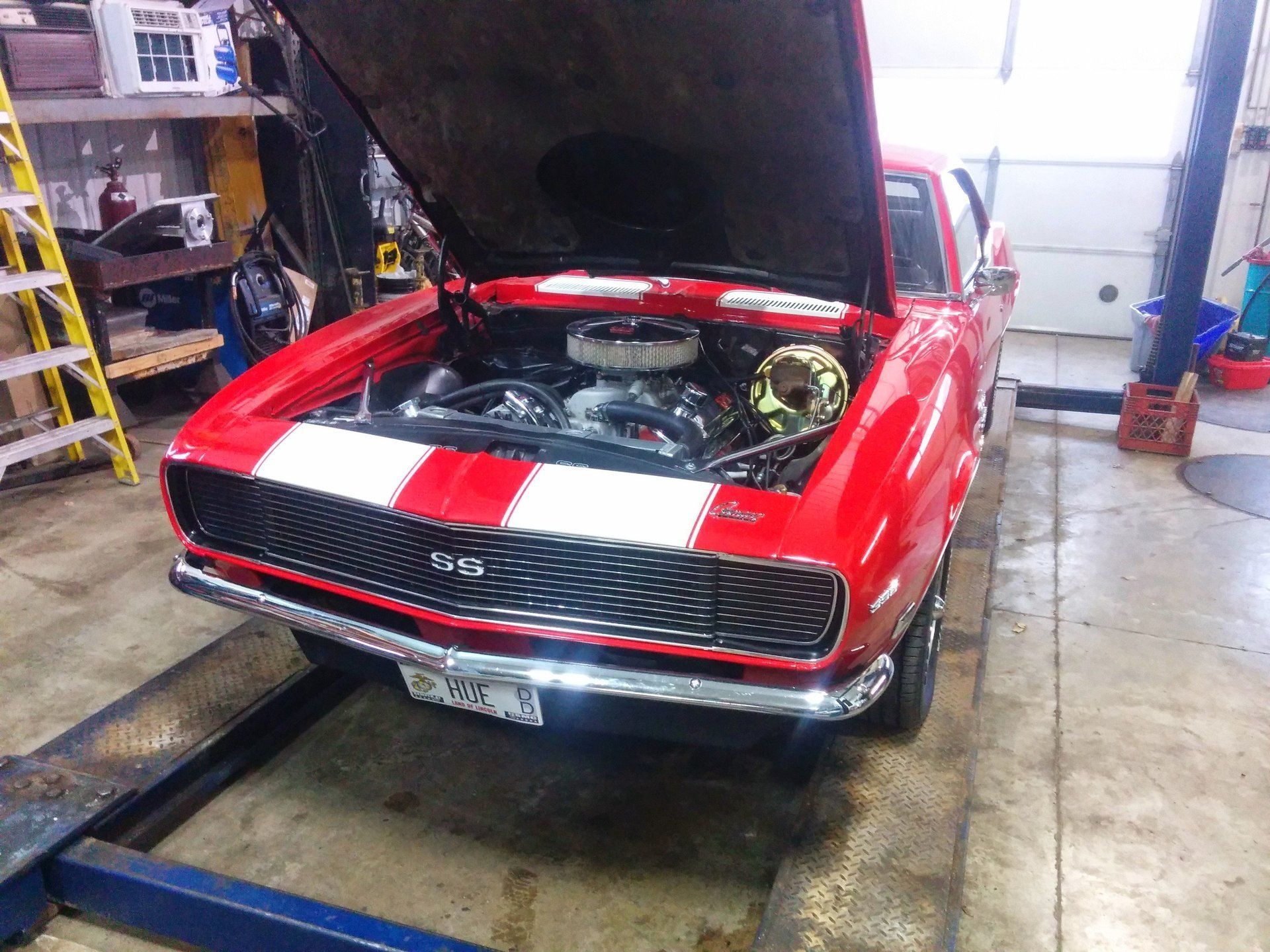Red classic muscle car with hood open in a garage, showing the engine bay.