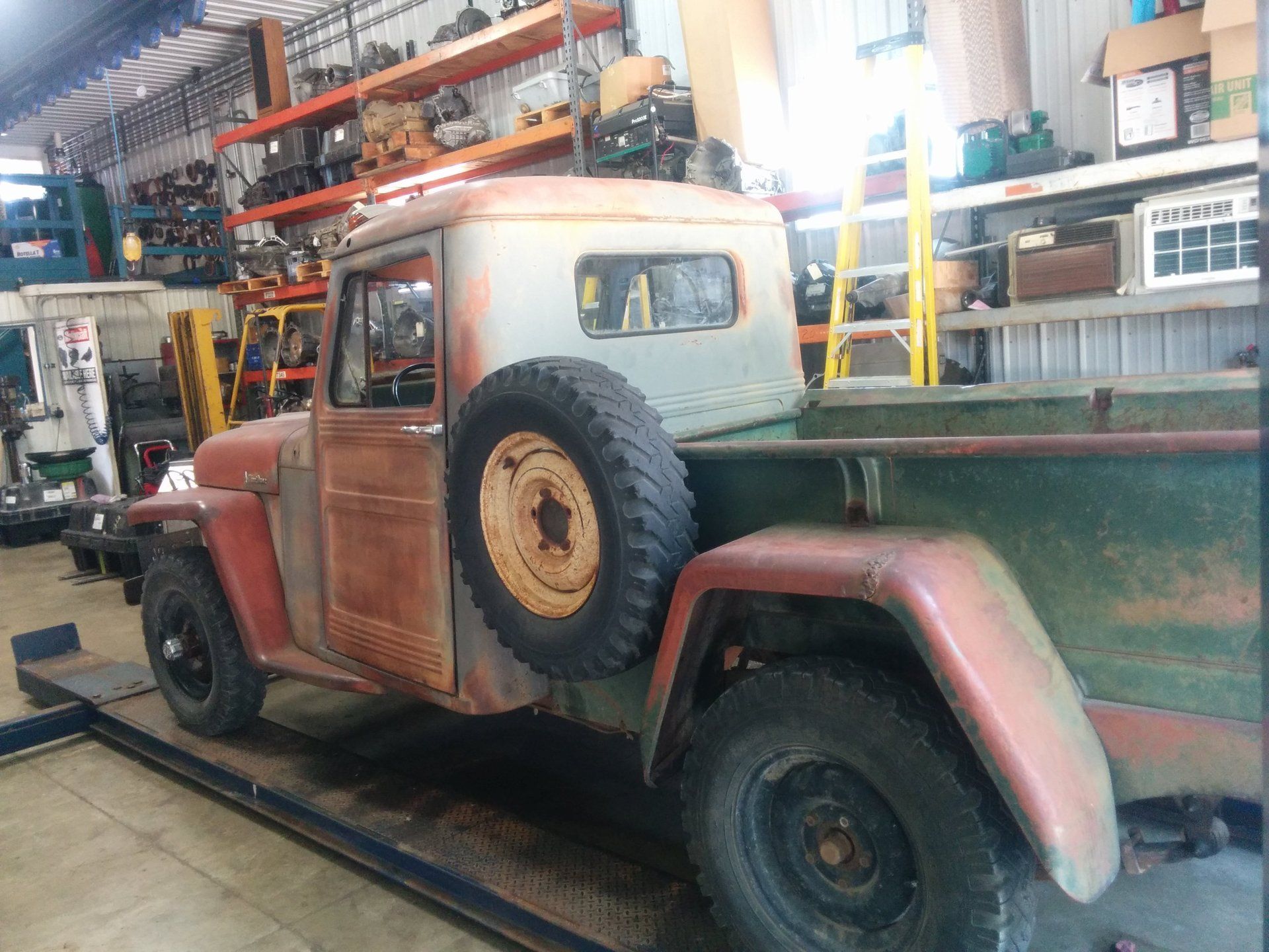 Old rusty flatbed pickup truck parked inside an industrial warehouse.