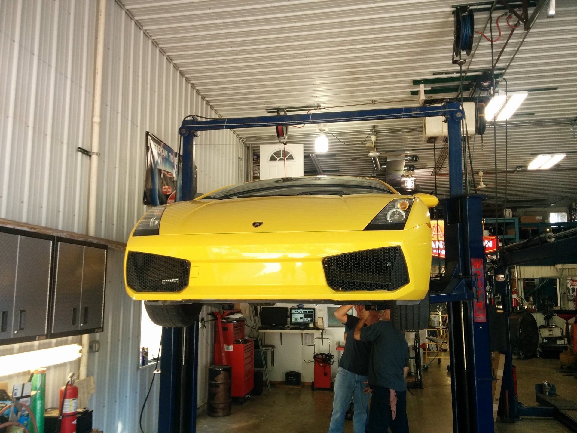 Yellow sports car lifted in an auto shop garage, front view with mechanic beneath it