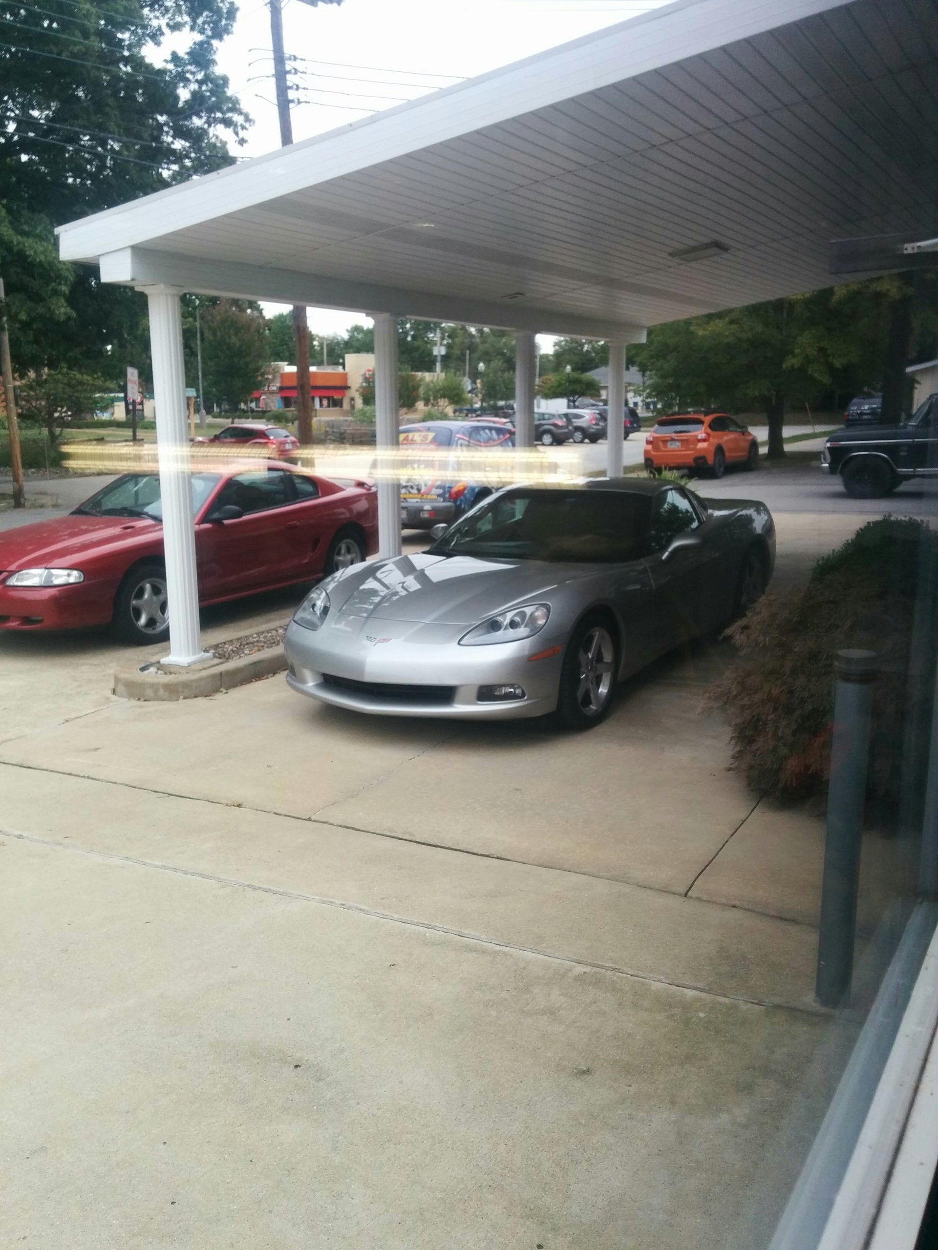 Silver sports car parked under a covered area beside a red car on a wet sidewalk