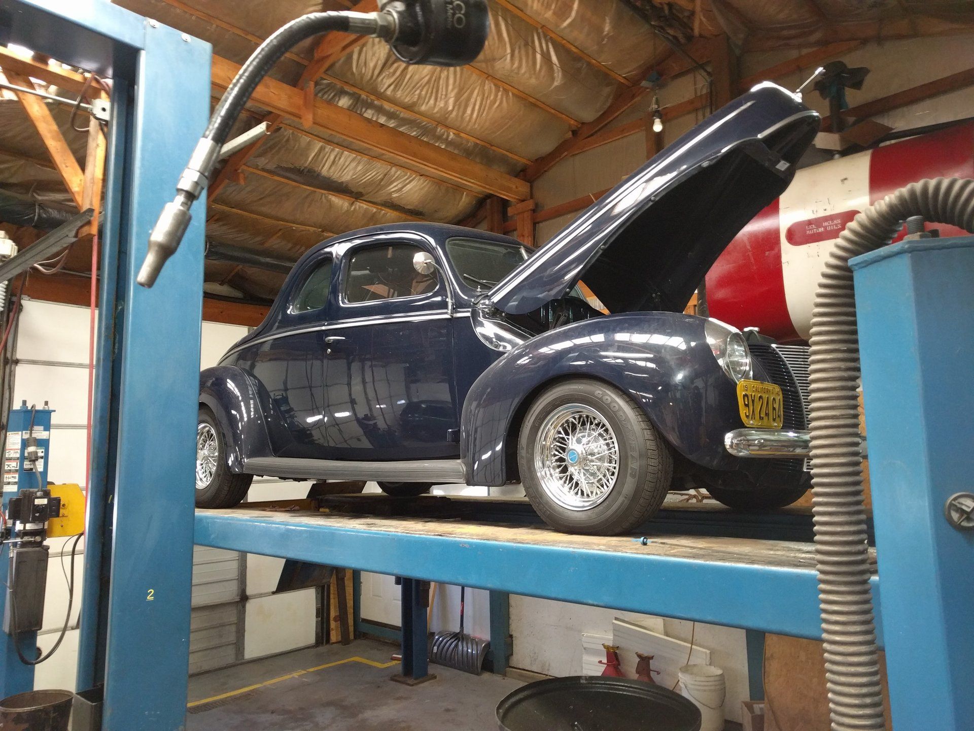 Classic Volkswagen Beetle on a car lift in a garage, hood open for maintenance.