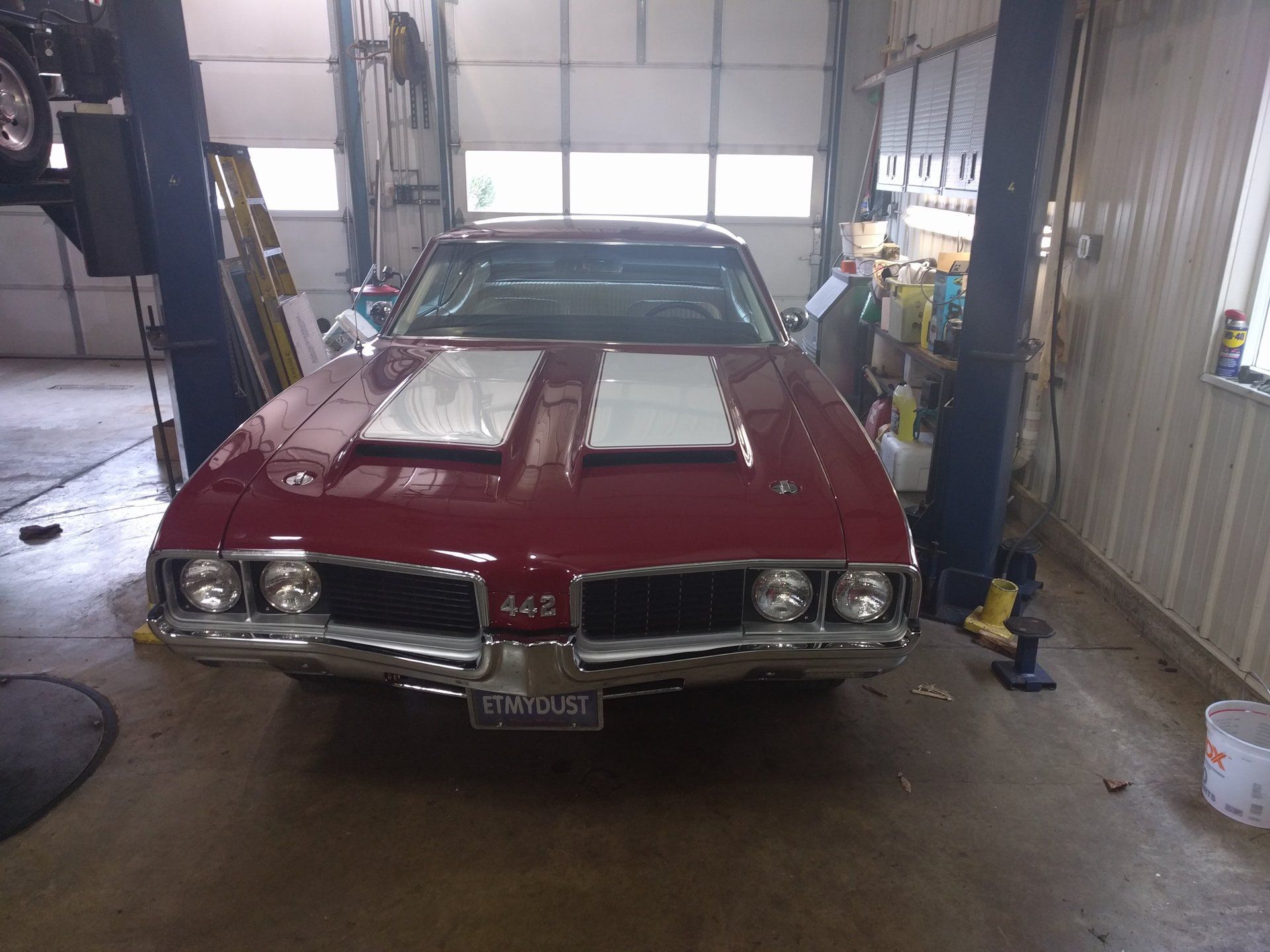Red classic car in a garage with its hood open, seen from the front.