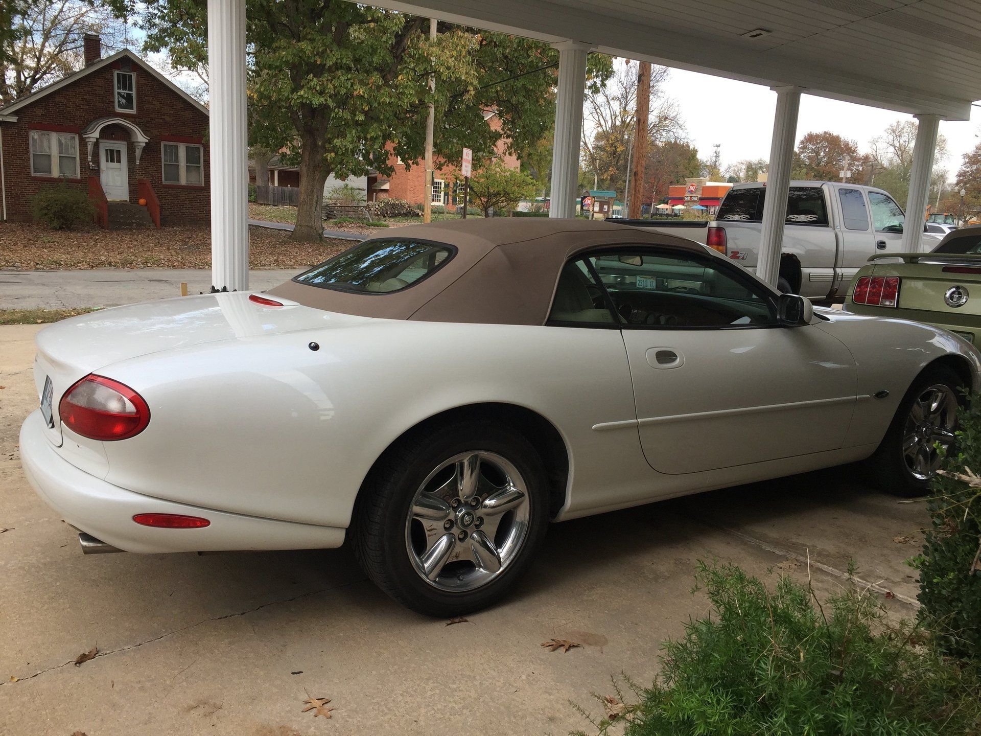 White convertible car parked in a driveway under a carport, with a tan top and chrome wheels.
