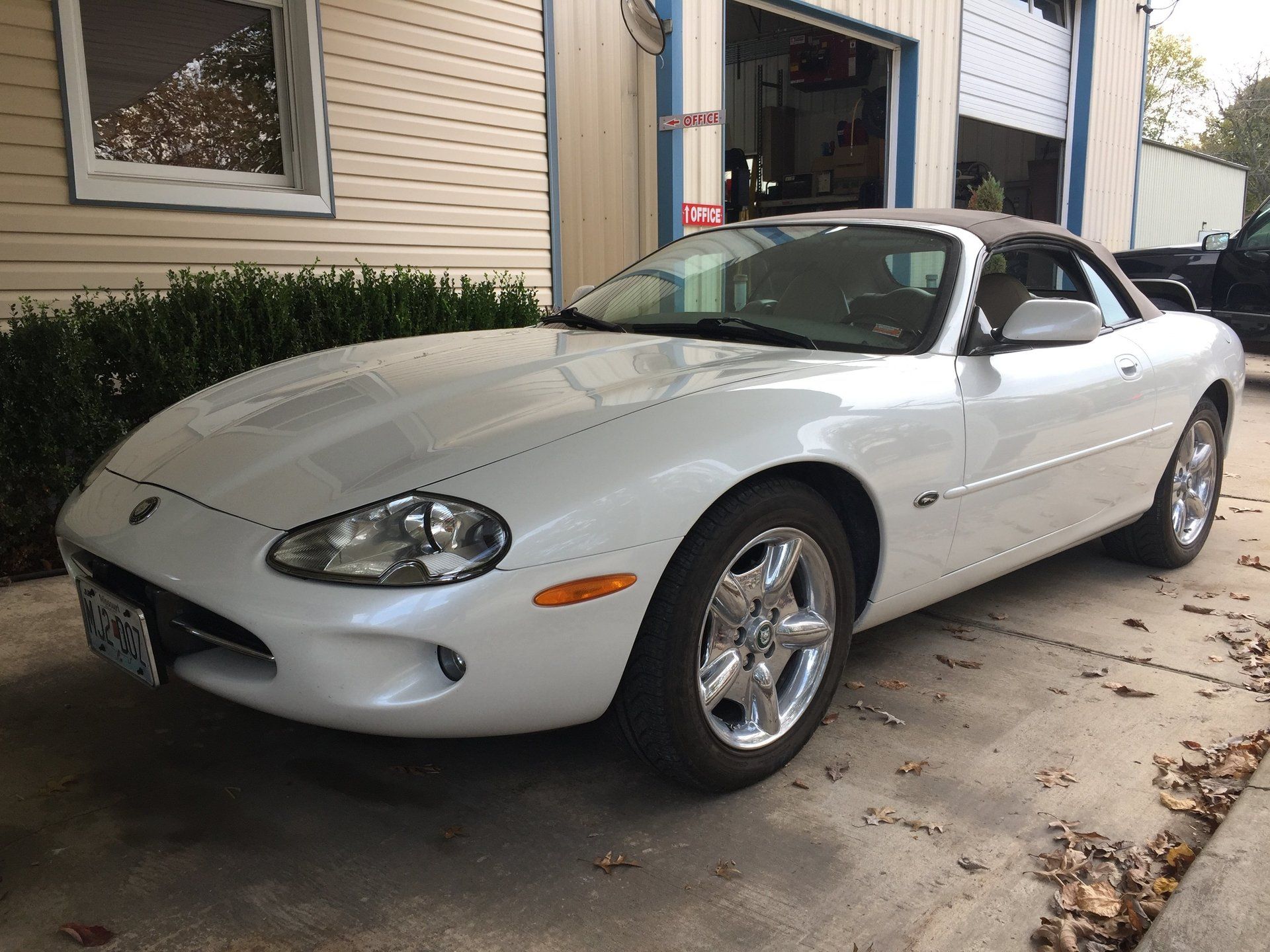White convertible sports car parked beside a building with an open garage door