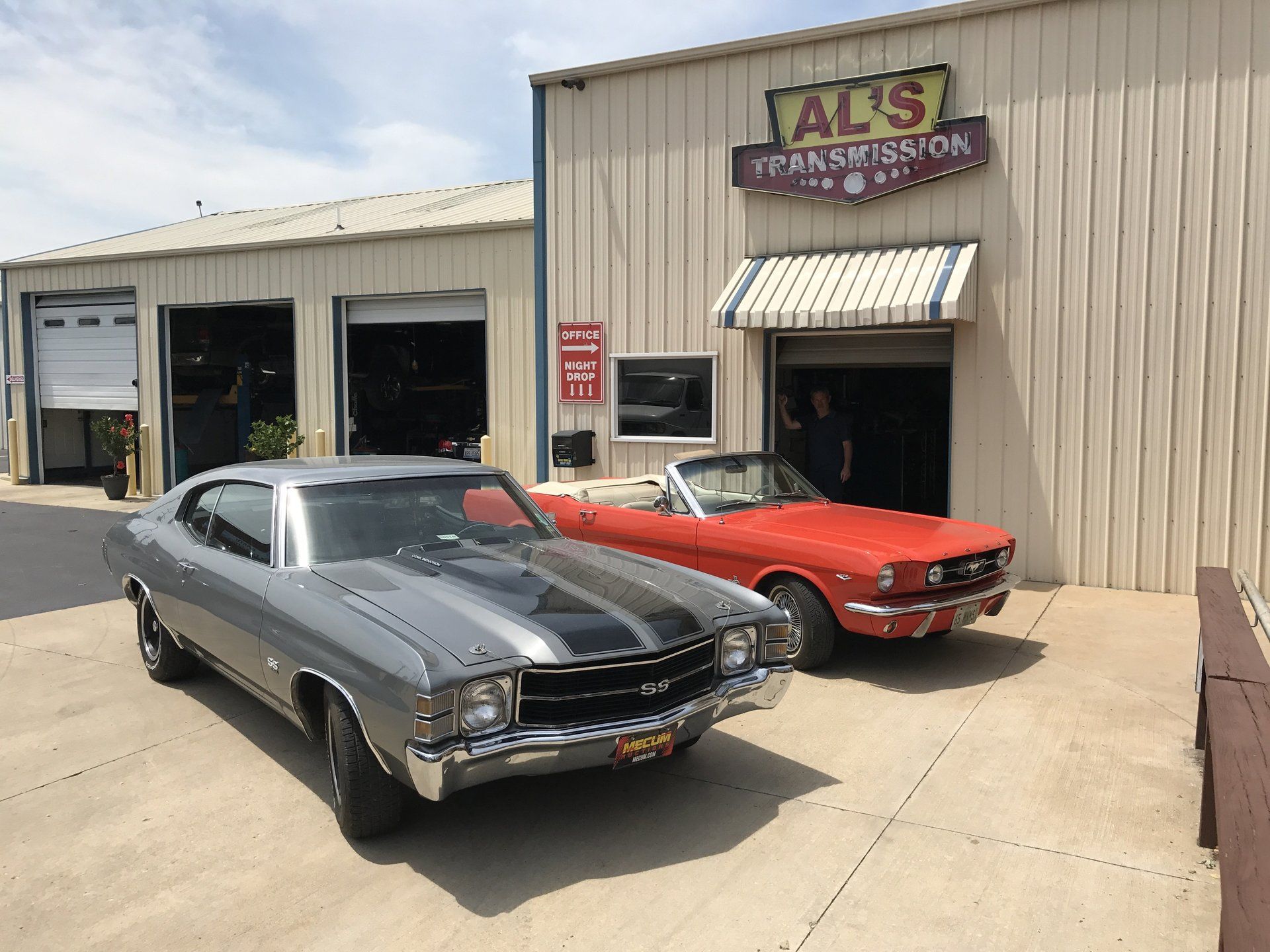Two classic cars parked outside Al's Performance shop on a sunny day.