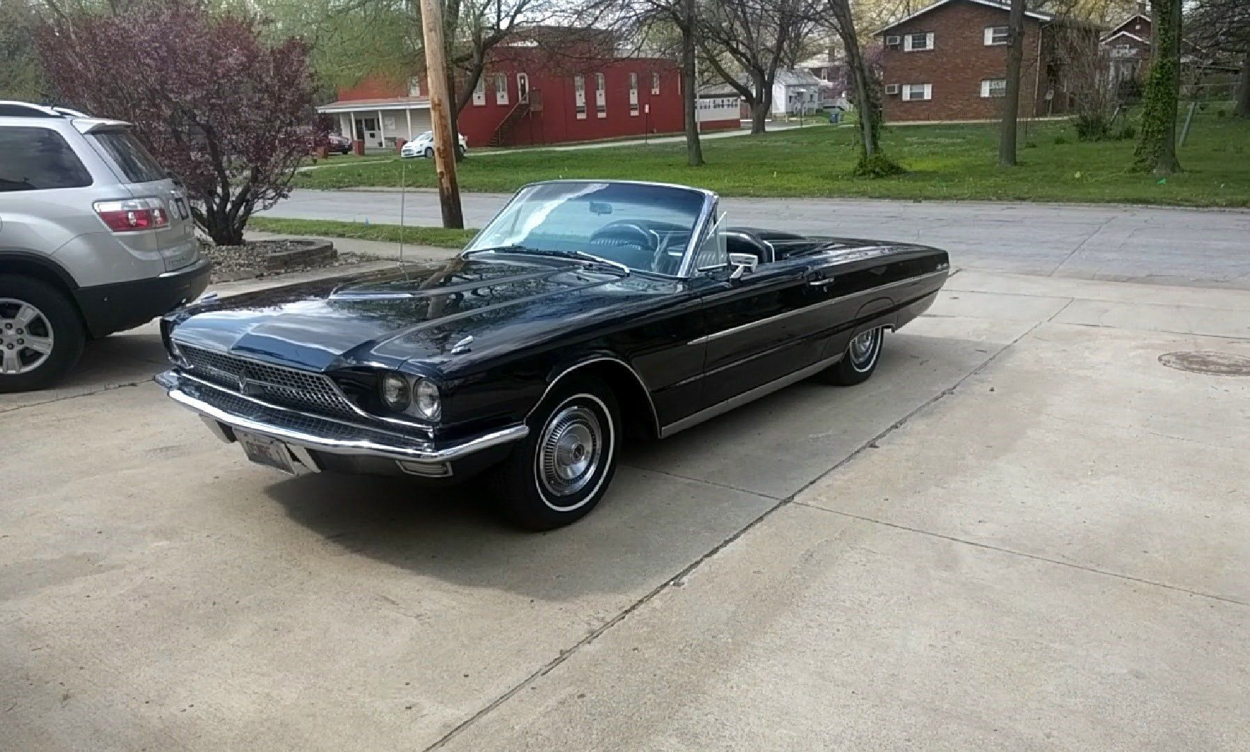 Black classic convertible parked on a driveway in a suburban neighborhood.