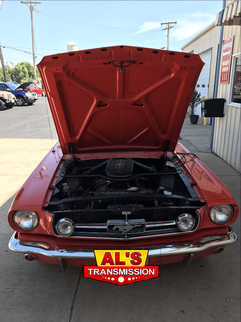 Red classic car with hood open at a transmission shop.