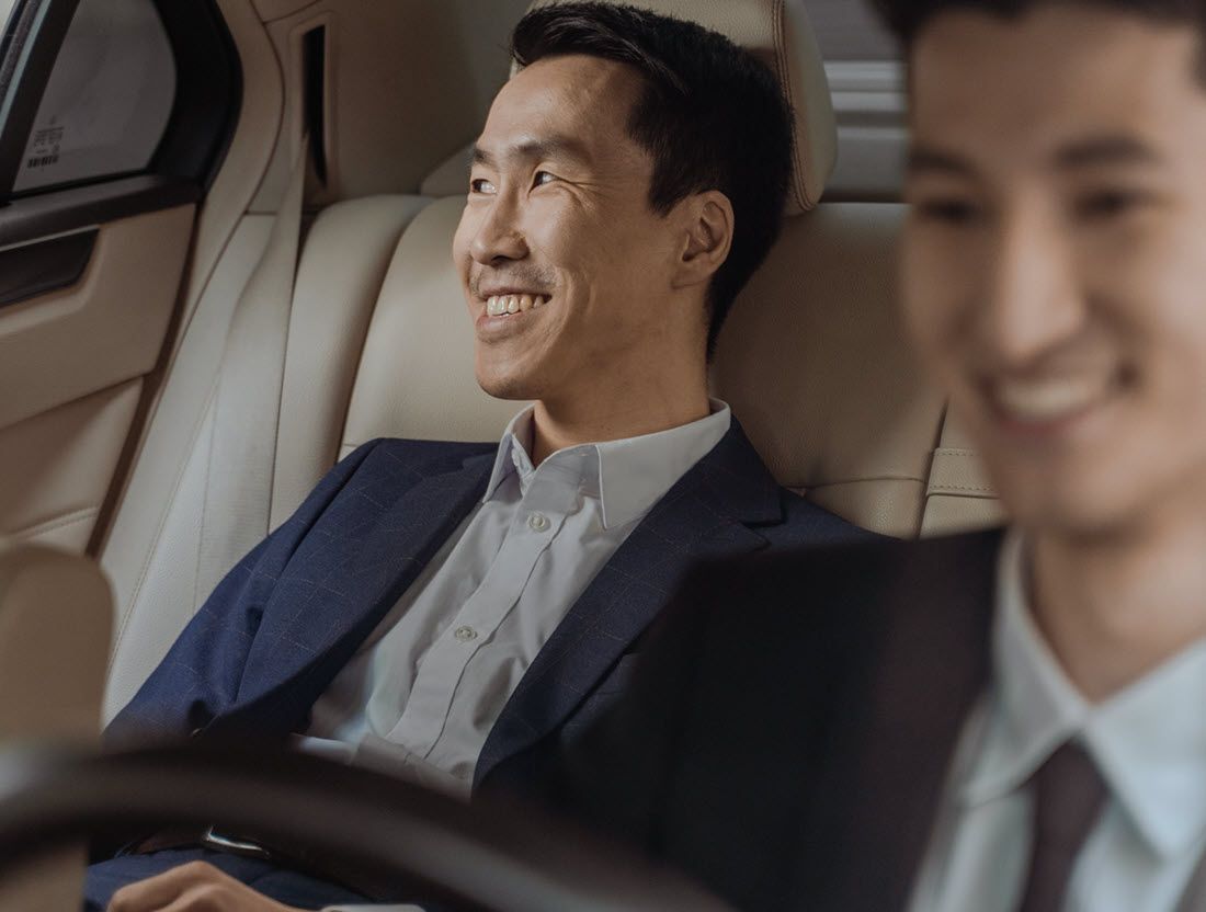 Two men in business suits smiling inside a luxury car, with one in the foreground blurred.
