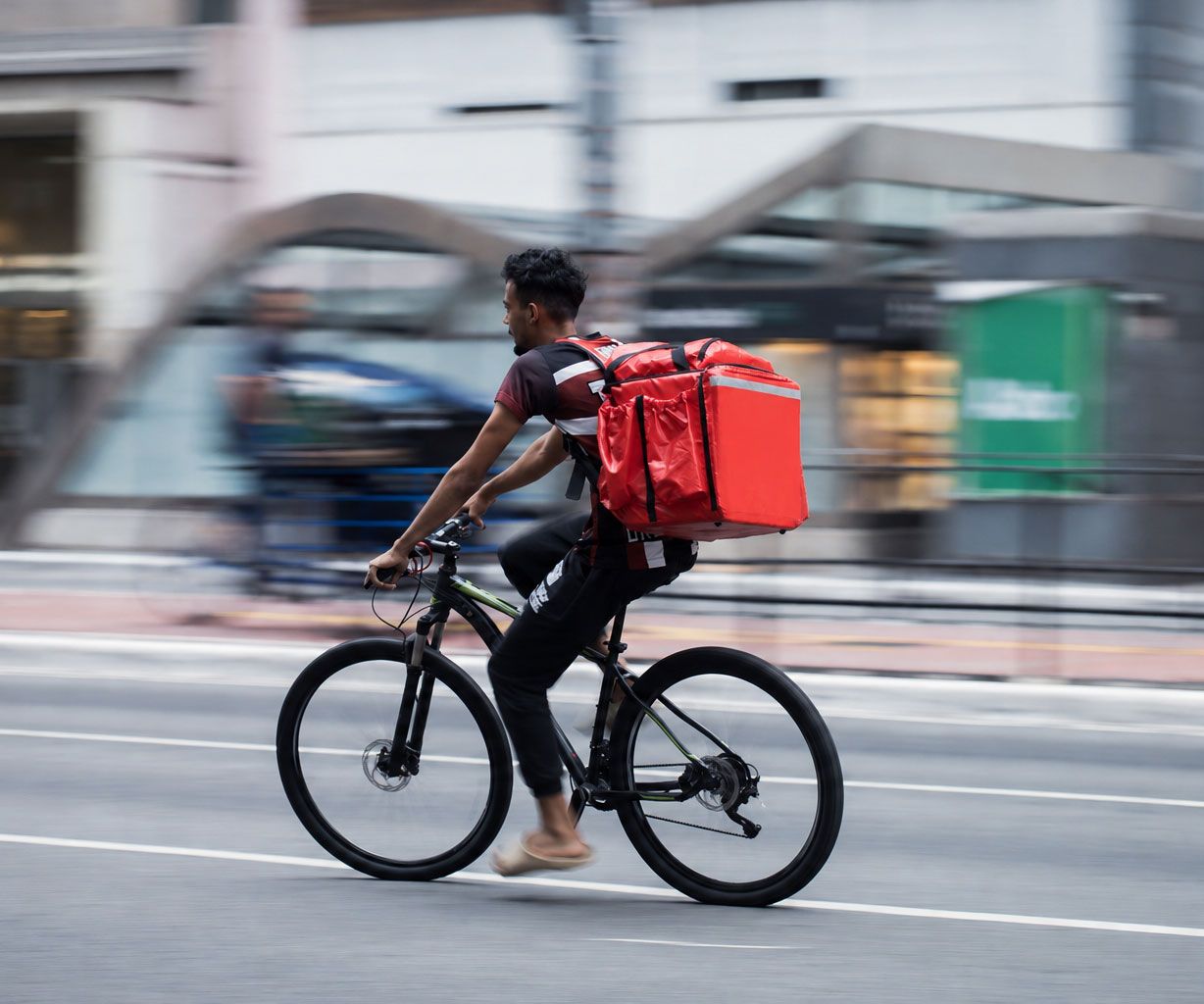 Cyclist riding a bike on a city street, wearing a large red delivery backpack.