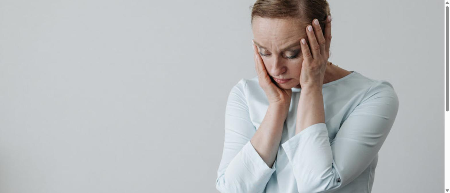 Worried woman holding her head with both hands against a gray background