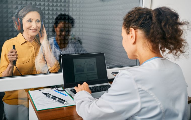Woman undergoing hearing test in soundproof booth with audiologist.