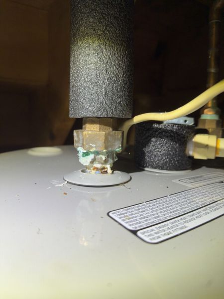 Close-up of a white water heater with a valve, pipe, and warning label underneath.