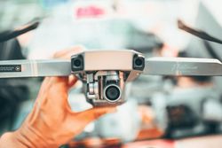 Drone being held up in a workshop, with a camera and blurred hands in the background