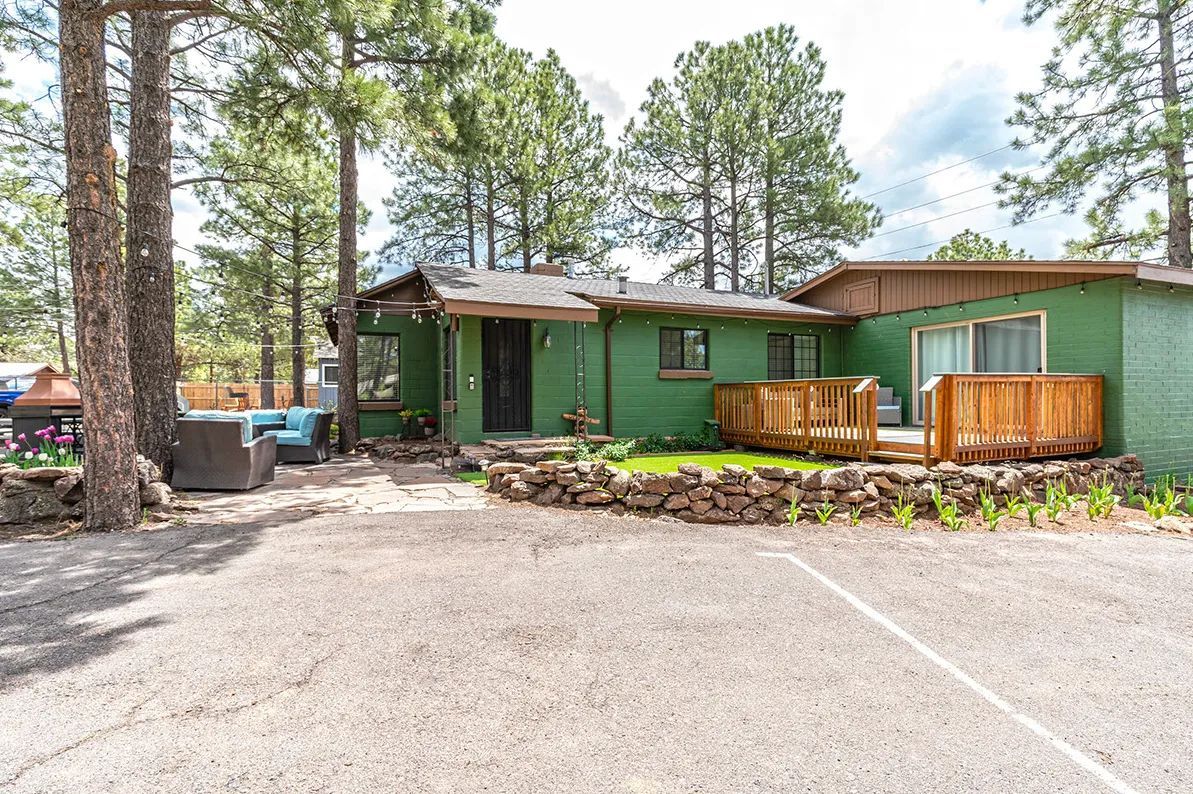 Green cabin with wooden deck and stone landscaping in a forested parking area