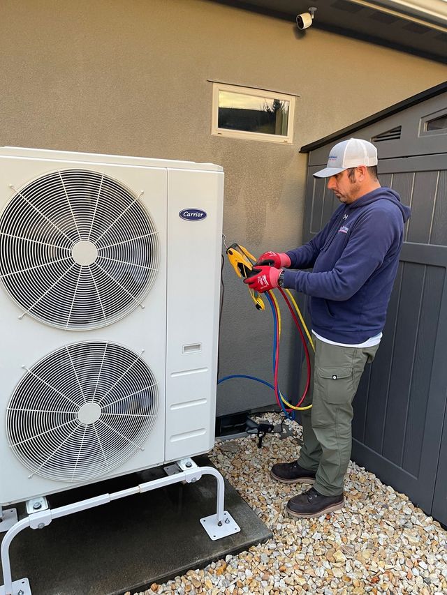 A man in a blue shirt and hat is fixing an air conditioner.