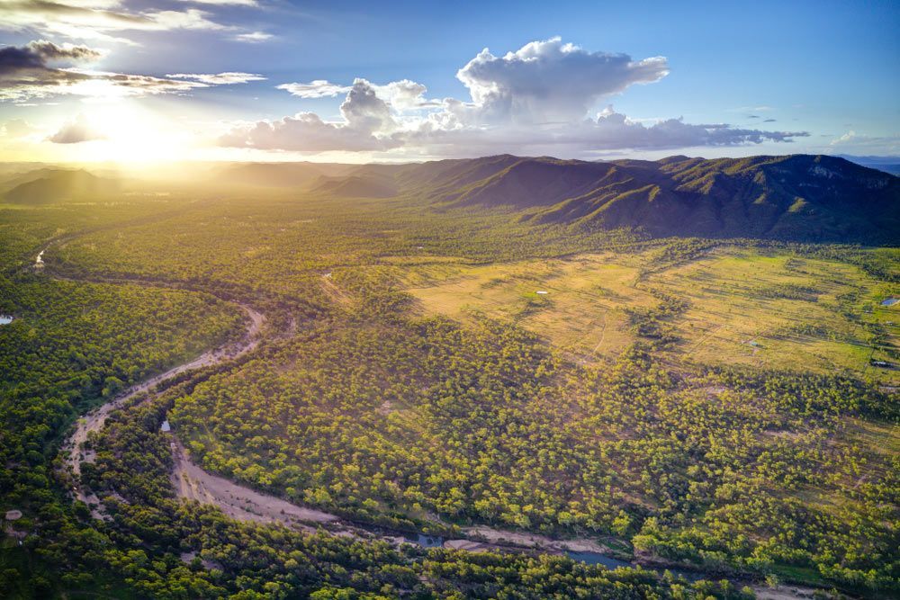 An Aerial View of A River Running Through a Lush Green Forest at Sunset — Conveyor Maintenance Services In Charters Towers, QLD