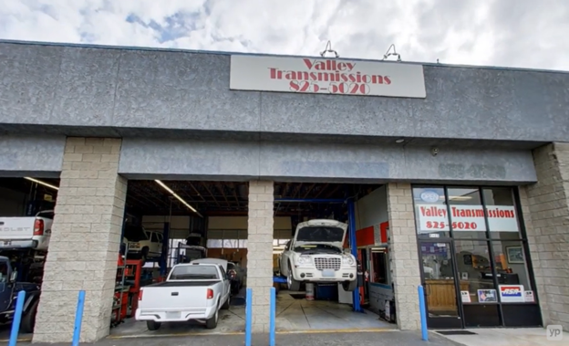 Auto repair shop with cars inside and a white SUV parked at the entrance under a signboard.
