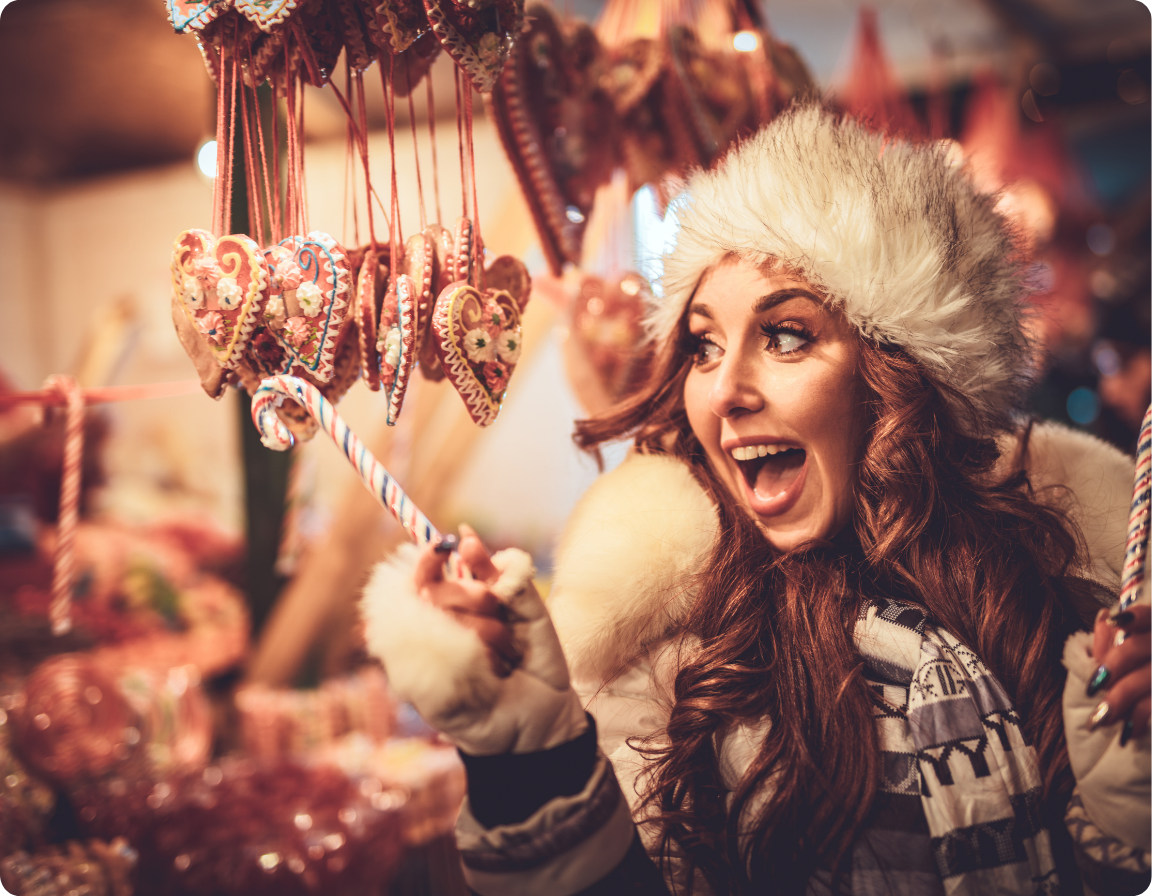 Woman in a fur hat smiling at a festive market stall with hanging heart ornaments