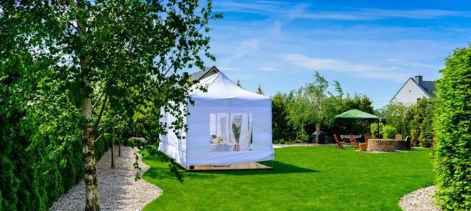 White garden marquee on a green lawn beside trees and a stone path under a blue sky