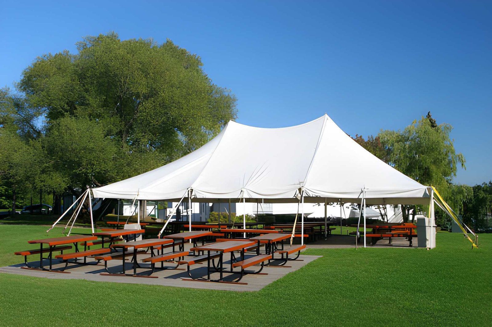 White event tent with picnic tables on a grassy field under a blue sky