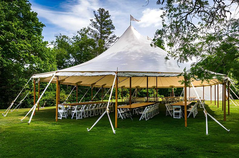 White tented outdoor pavilion with rows of chairs on green grass surrounded by trees
