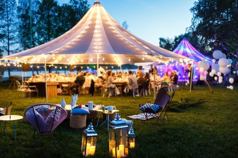 Lit outdoor wedding reception under a large white tent with glowing lanterns and string lights at dusk