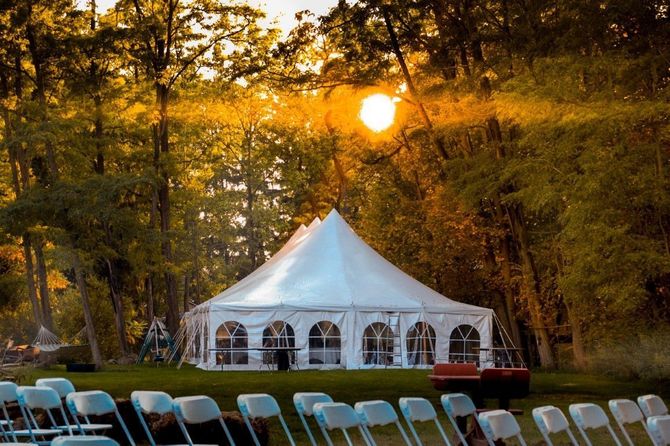 White event tent at sunset in a wooded clearing with rows of chairs in front