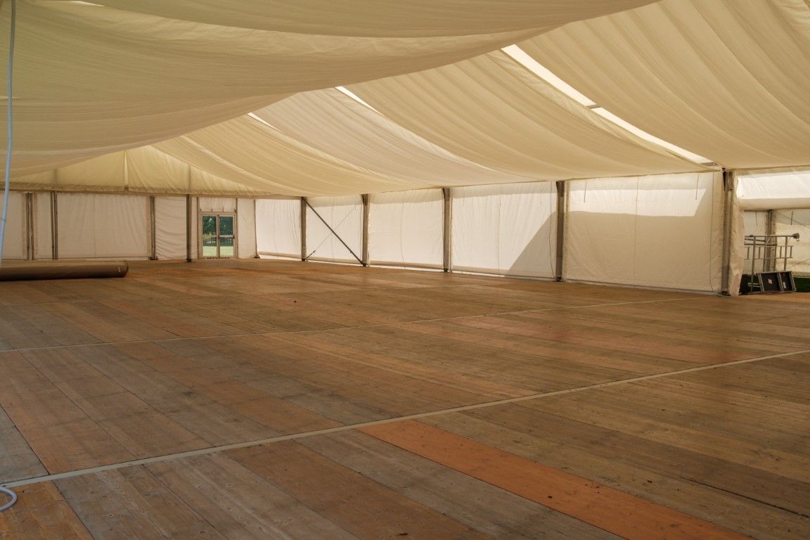 Empty indoor tent with a large beige fabric ceiling and wooden floor panels
