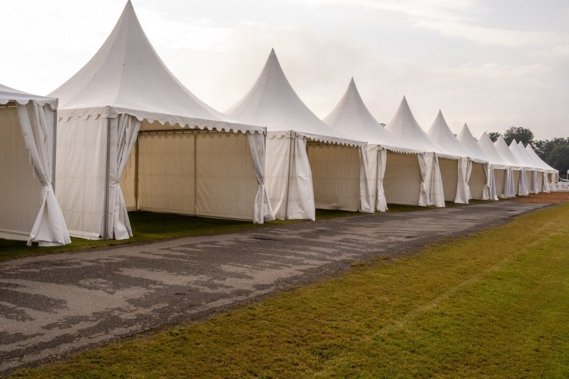 Row of white event tents along a gravel path beside a grassy field