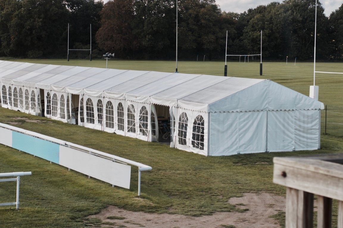 White tent beside a sports field, with long benches in the foreground and trees in the background