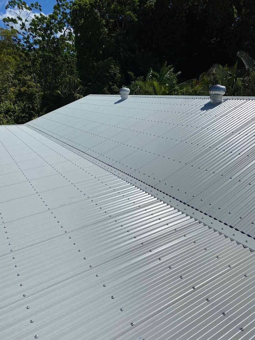 A White Corrugated Metal Roof With Trees In The Background — Posty’s Roofing In Airlie Beach, QLD