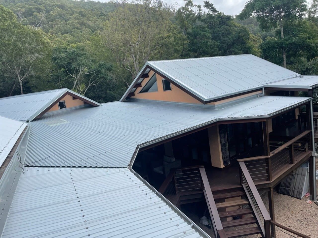 A House With A Metal Roof Is Surrounded By Trees — Posty’s Roofing In Airlie Beach, QLD