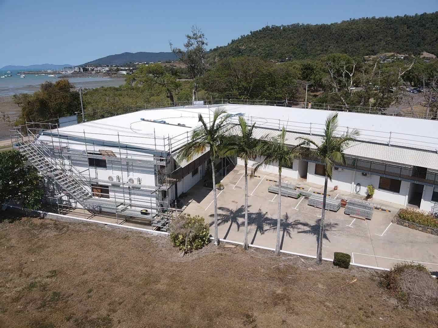 An Aerial View Of A Building With Palm Trees In Front Of It — Posty’s Roofing In Cannonvale, QLD