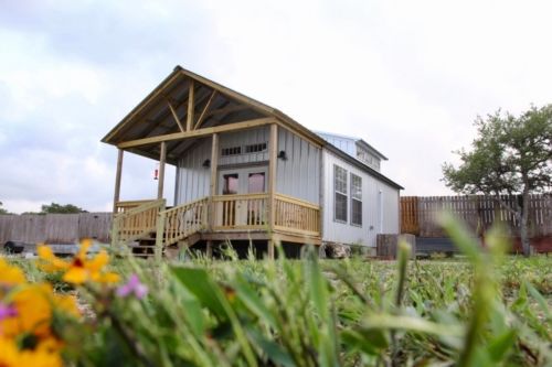 a small house with a porch is sitting in the middle of a grassy field .