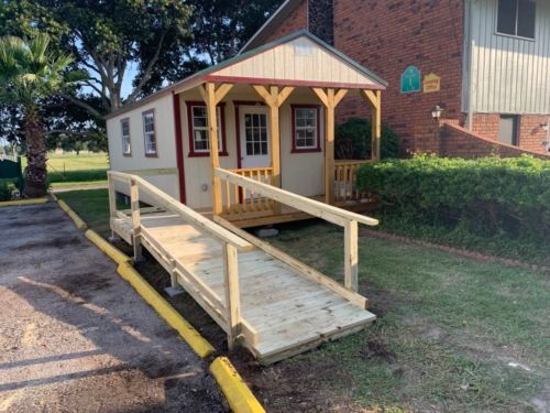 a small house with a ramp and a porch in front of a brick building .