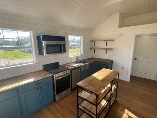 a kitchen with blue cabinets , stainless steel appliances , a sink , stove and microwave.