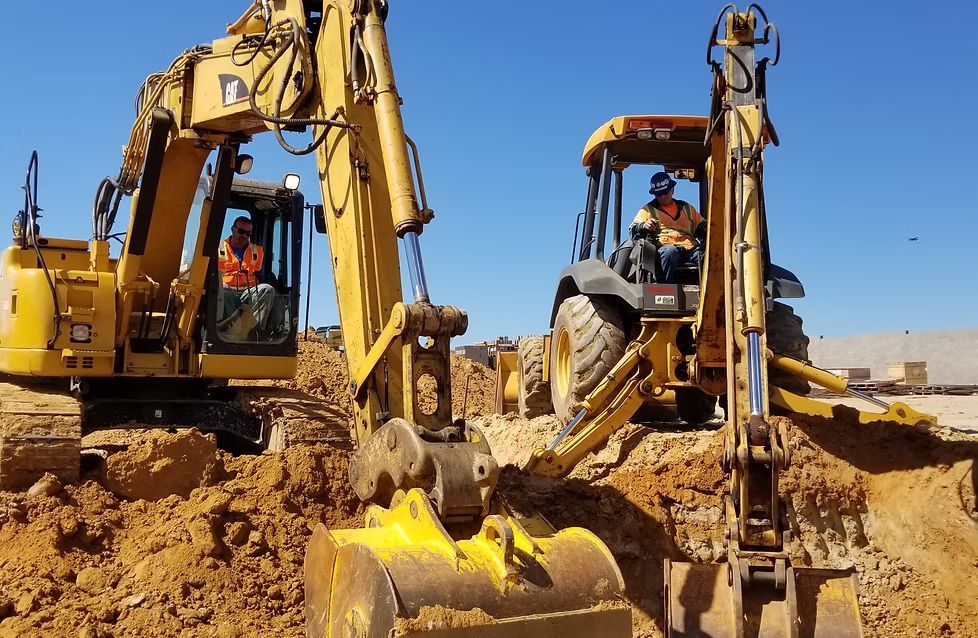 Yellow excavator and backhoe digging in a construction site on a sunny day.