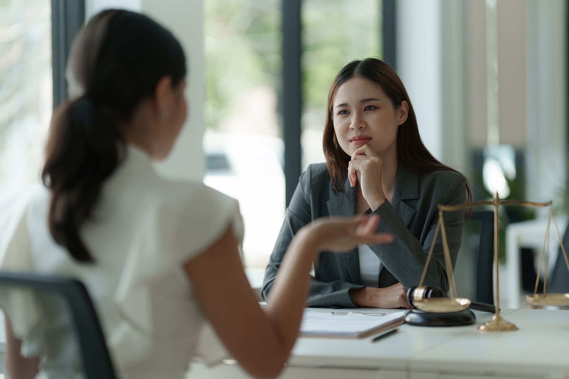 Two people in a bright office discuss documents across a desk, one listening thoughtfully.