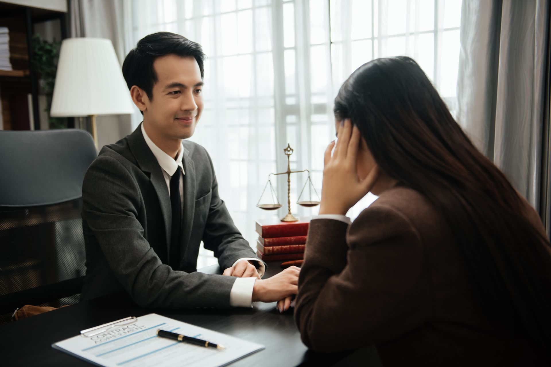 Two people in a meeting across a desk, one speaking and the other listening in an office.