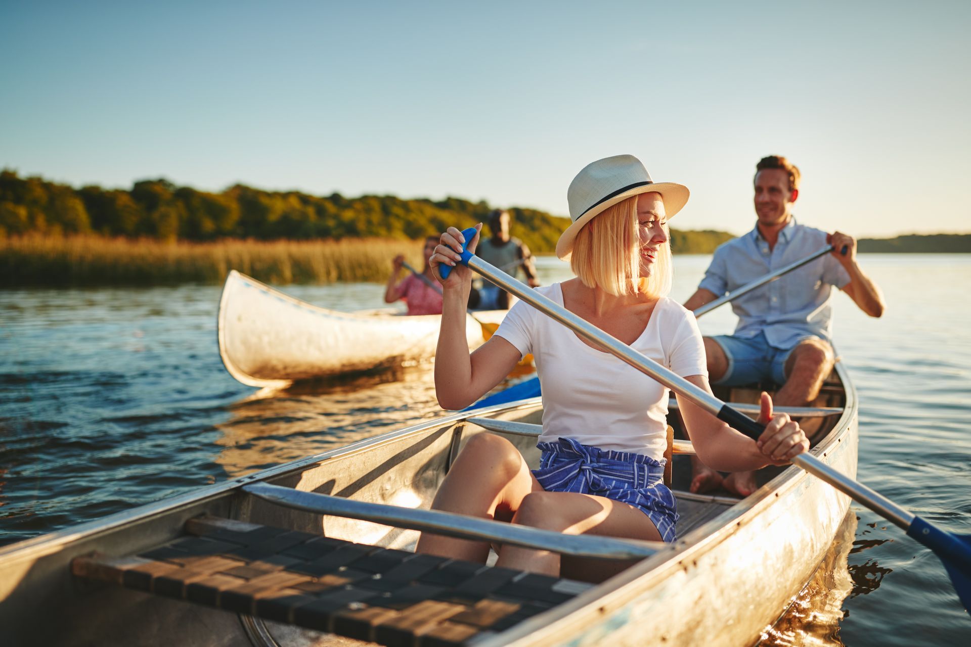 People canoeing on a calm river at sunset, with one person paddling in the foreground.