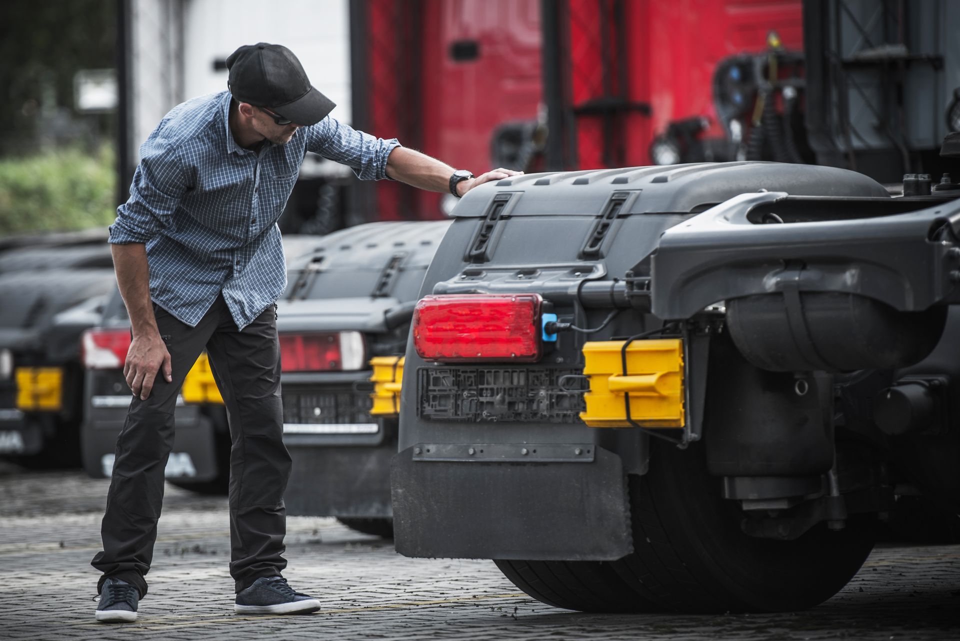 Man inspecting the rear bumper of a black sports car on a cobblestone street, with several cars parked behind.