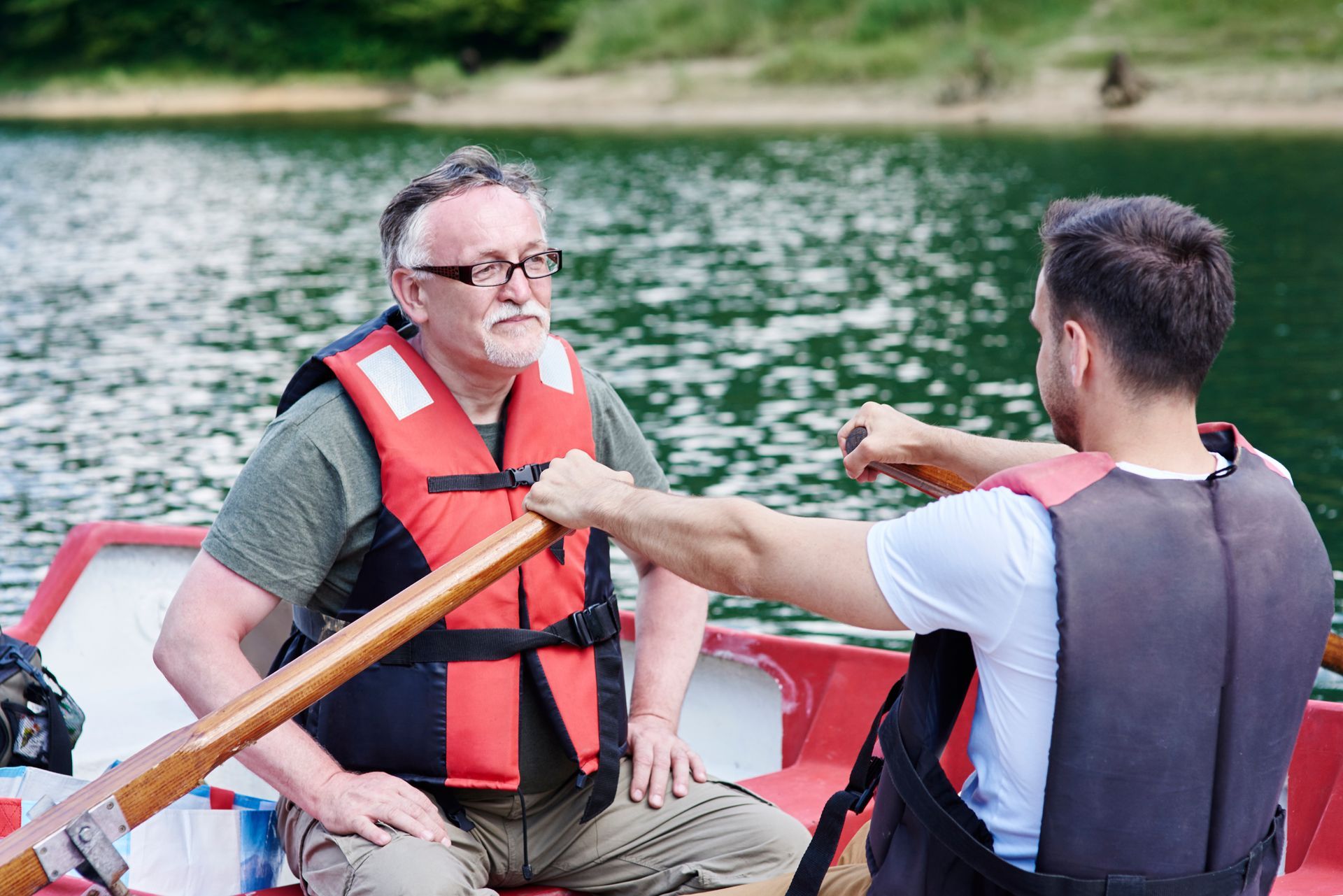 Two men in life vests rowing a small boat on a lake
