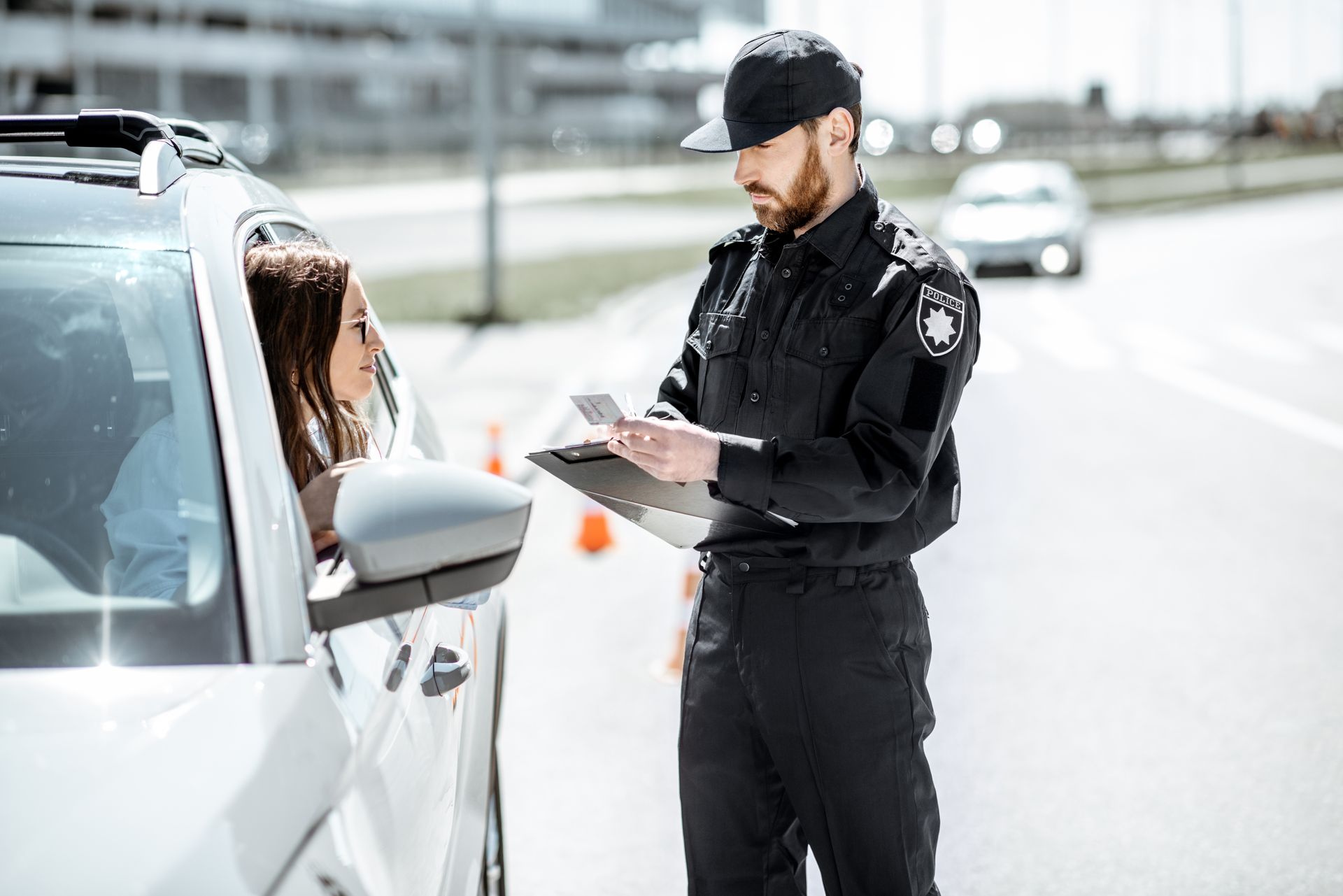 Police officer checking documents beside a white car on a roadside