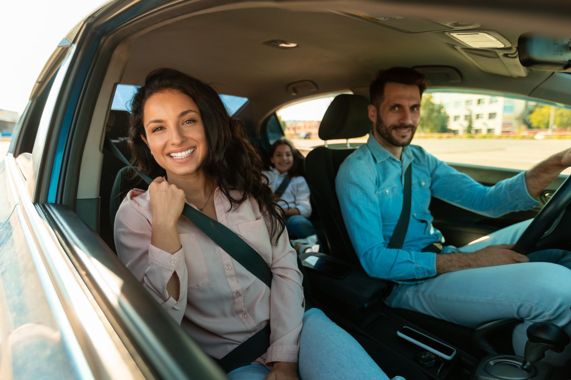 Smiling family riding in a car, with front-seat passengers and a child in the back seat.