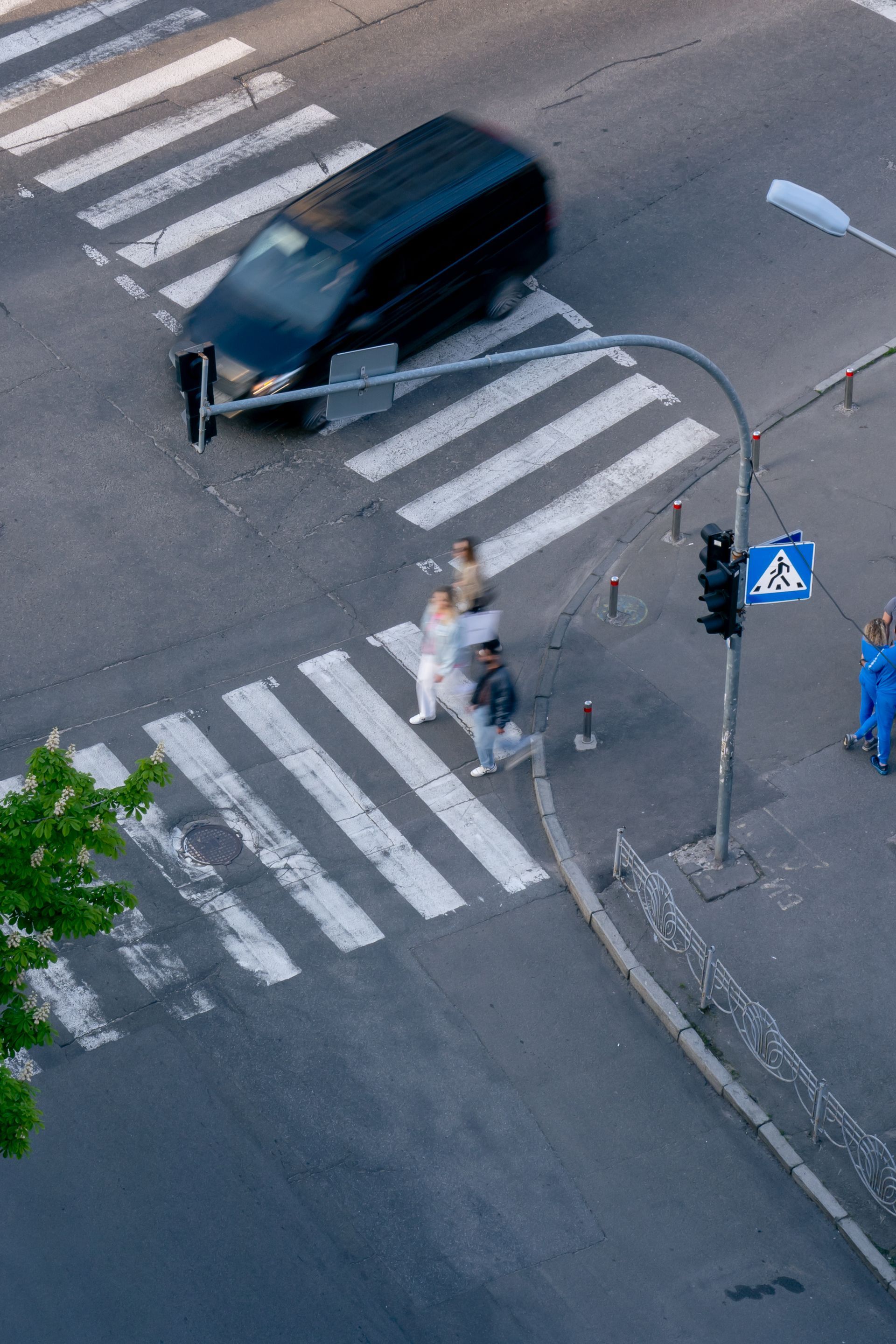Two people crossing a street at a crosswalk beside a black van on a city intersection
