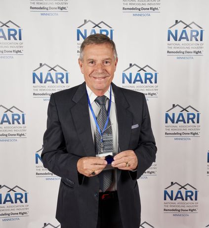 Man in suit smiling, holding a blue badge in front of a blue and white NARI backdrop.