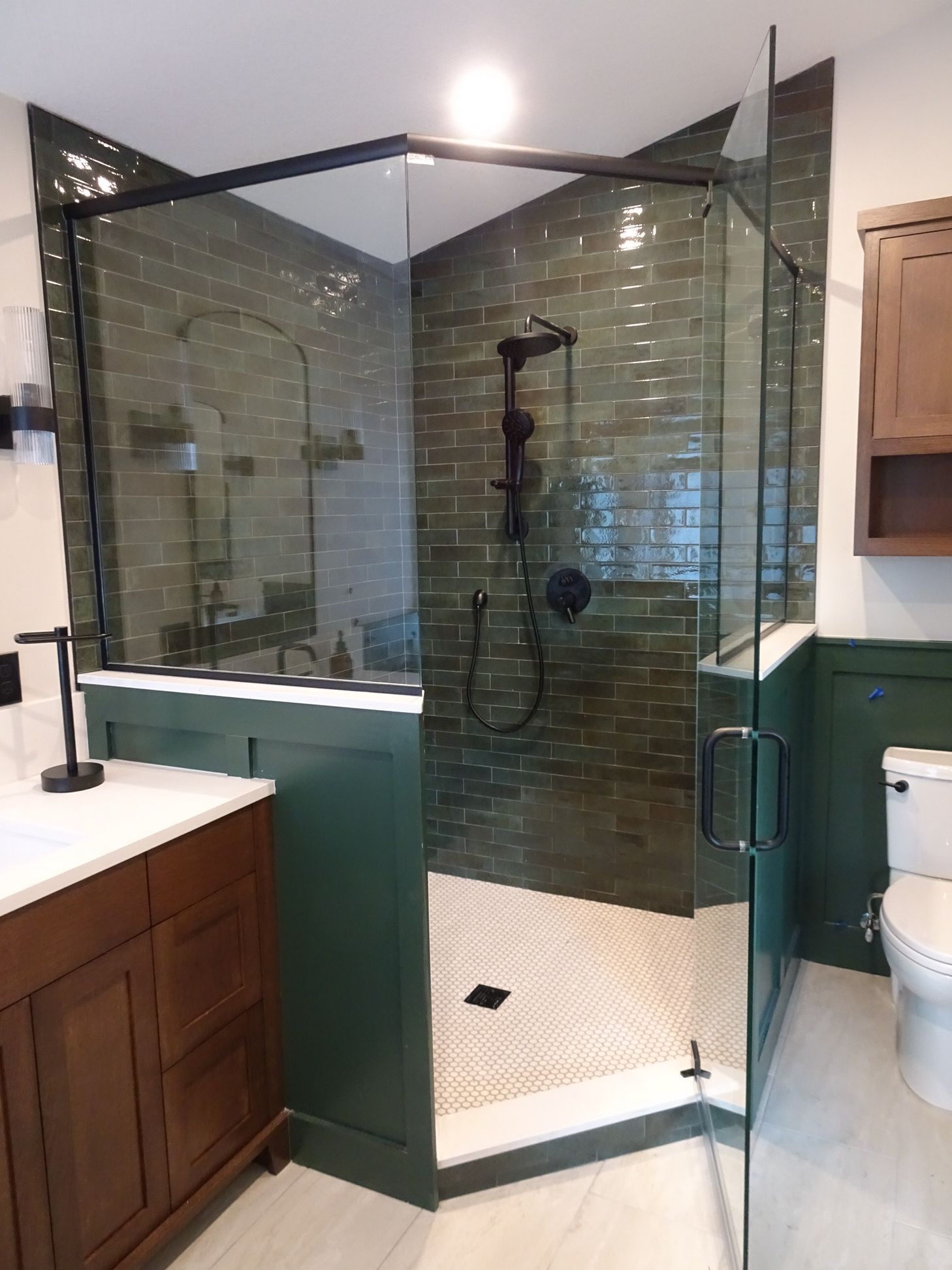 Corner glass shower enclosure with black metal frame and handheld shower wand against green subway tile, primary bathroom remodel, Eden Prairie, MN