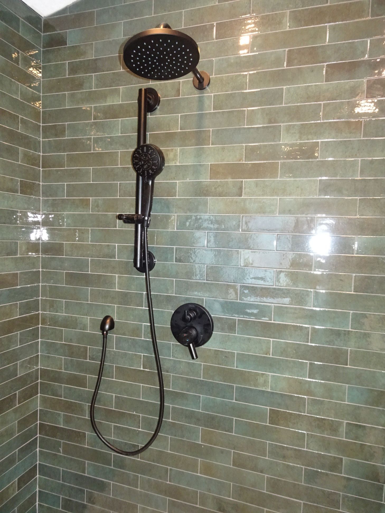 Black rain shower head and handheld wand against glossy green subway tile wall, primary bathroom remodel, Eden Prairie, MN