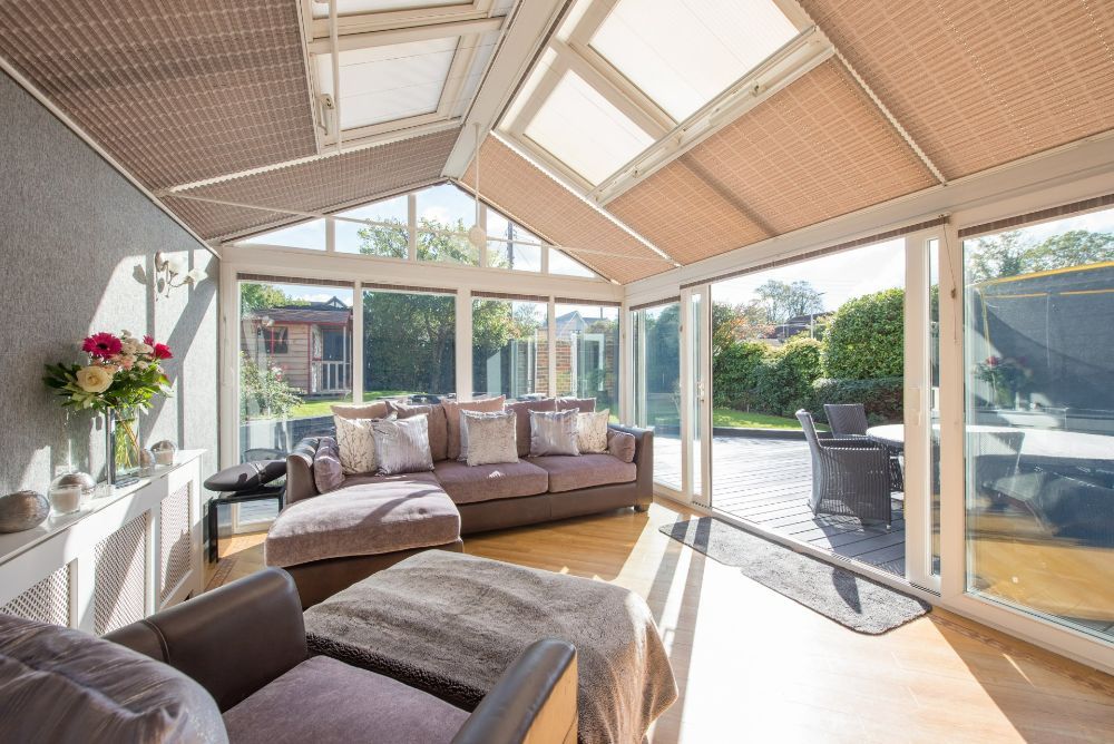 Sunroom with a brown sectional sofa, skylights, and a view of a patio and garden.